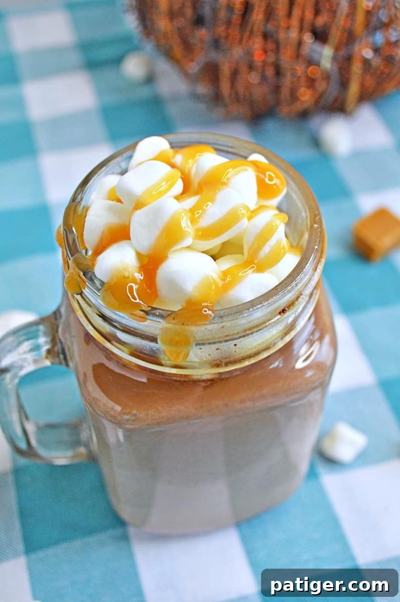 A close-up shot of a mug of slow cooker salted caramel hot chocolate, topped with generous whipped cream, a drizzle of caramel, and a sprinkle of sea salt. Emphasizing its rich and creamy texture.