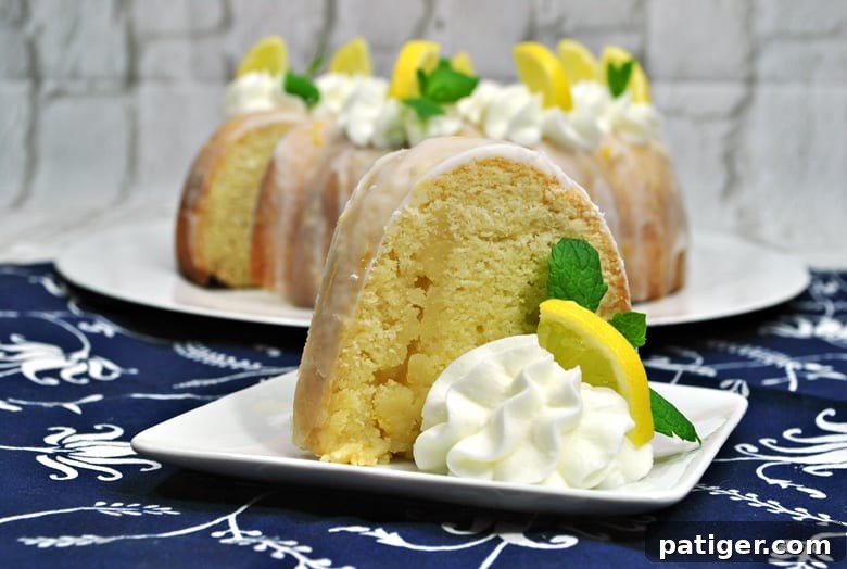 Zesty Lemon Bundt Bliss 2 Complete with a zesty lemon glaze, this homemade moist lemon bundt cake recipe is the perfect combination of sweet and tangy. A beautiful, golden-yellow bundt cake on a white cake stand, drizzled generously with glaze.