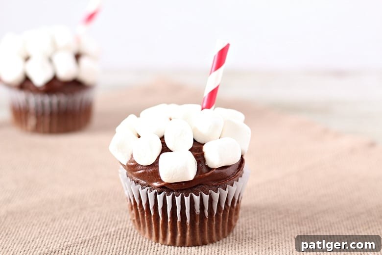 Cozy Cocoa Cloud Cupcakes 6 A finished Hot Chocolate Cupcake, adorned with chocolate icing, mini marshmallows, and a small paper straw inserted at an angle.