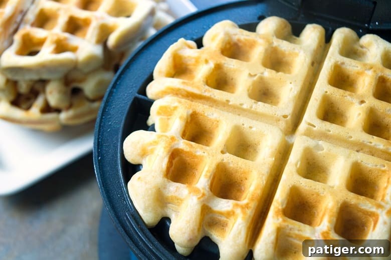 Reese's Puffs waffles cooking in a waffle iron, showcasing their golden-brown color and inviting texture as they reach perfect crispiness.