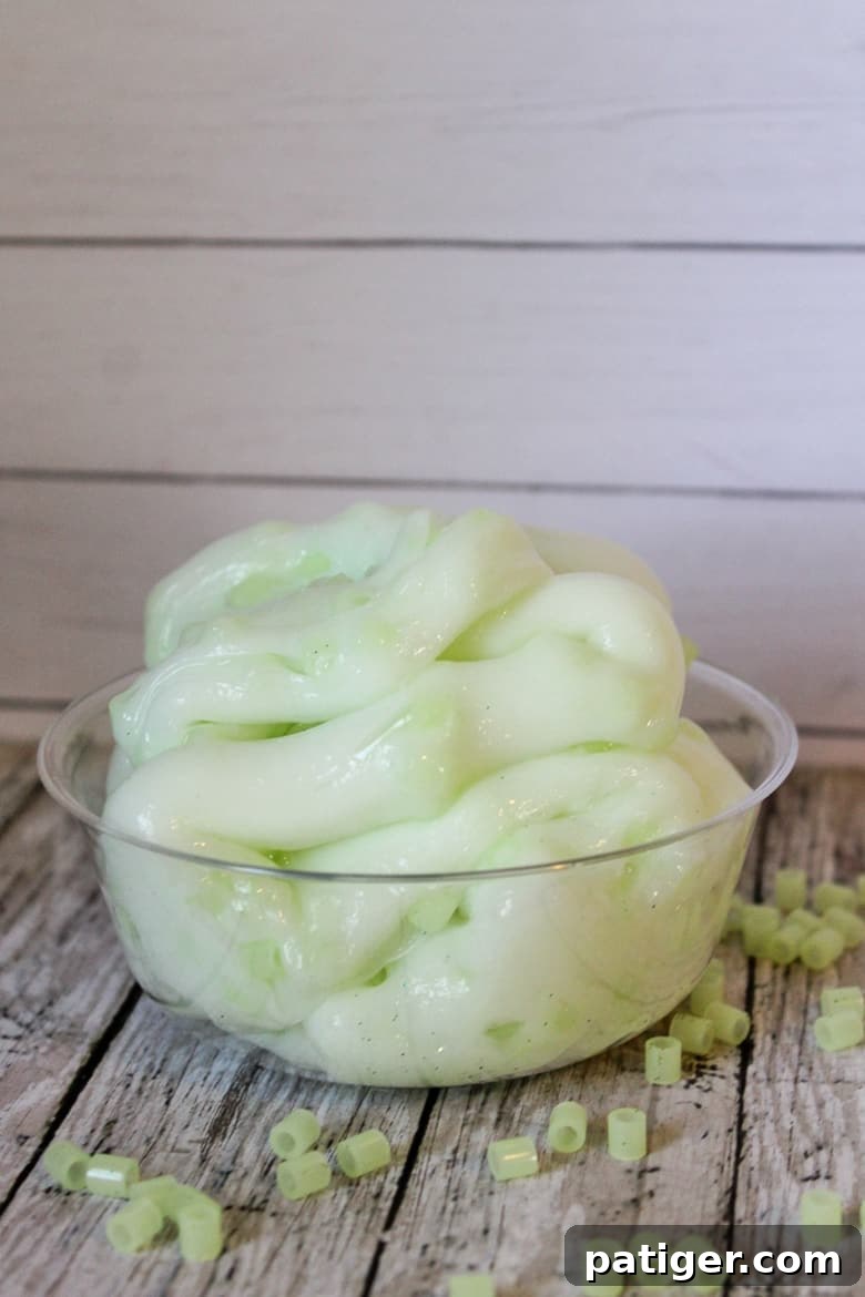 A bowl of vibrant green glow in the dark crunchy slime surrounded by loose glow in the dark Perler beads on a rustic wooden surface.