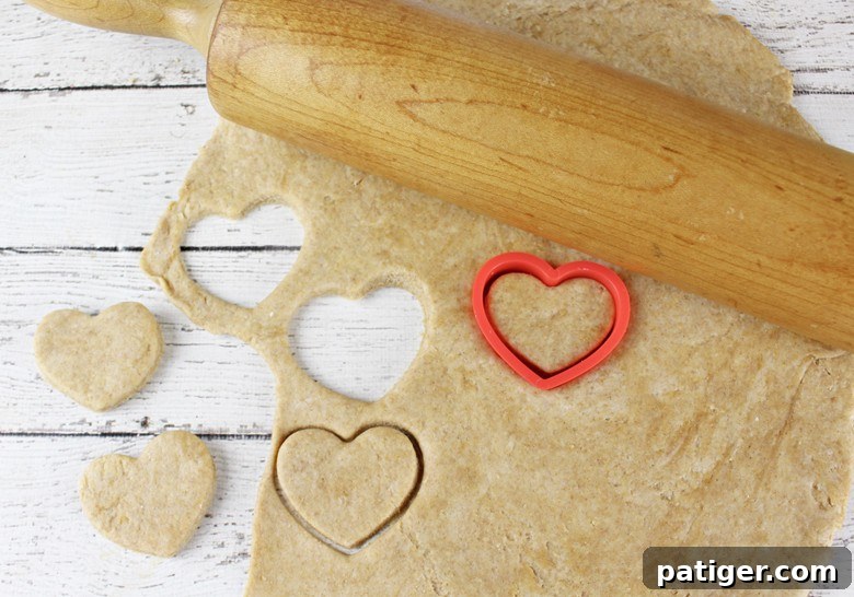Dog treat dough rolled out on a surface with heart-shaped treats being cut out using a cookie cutter and rolling pin.