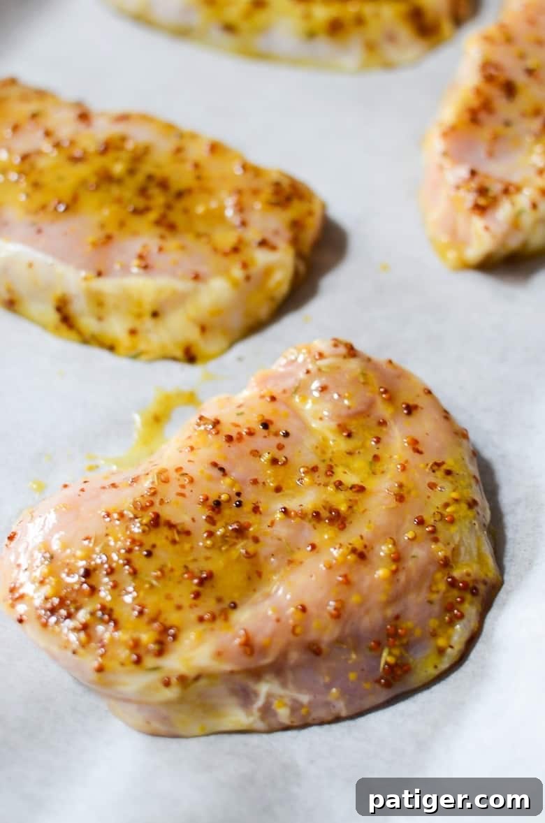 Uncooked honey mustard pork chops perfectly arranged on a lined baking sheet, ready for the oven.