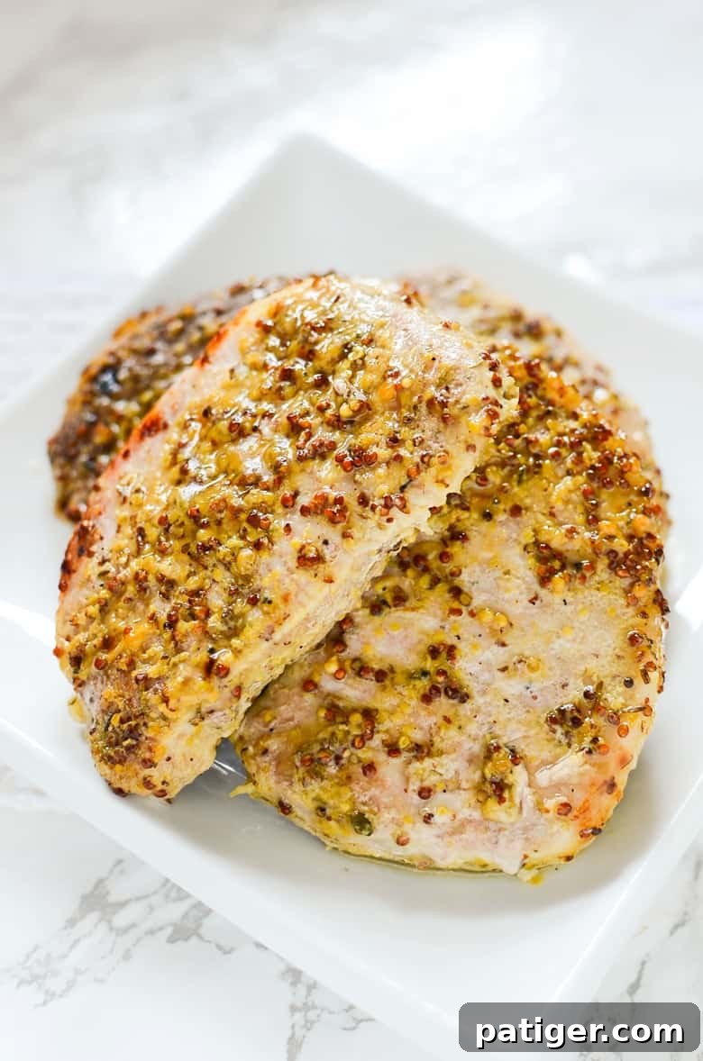 Oven Roasted Pork Chops with Grainy Mustard and Thyme, beautifully plated on a white dish with garnishes.