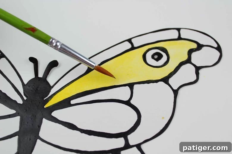 Stained Glass Style Butterfly Craft 7 A paintbrush applying yellow paint to butterfly