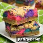 Two colorful layered dessert bars with bright pink, purple, and blue cheesecake swirls and cookie crumbles on top.