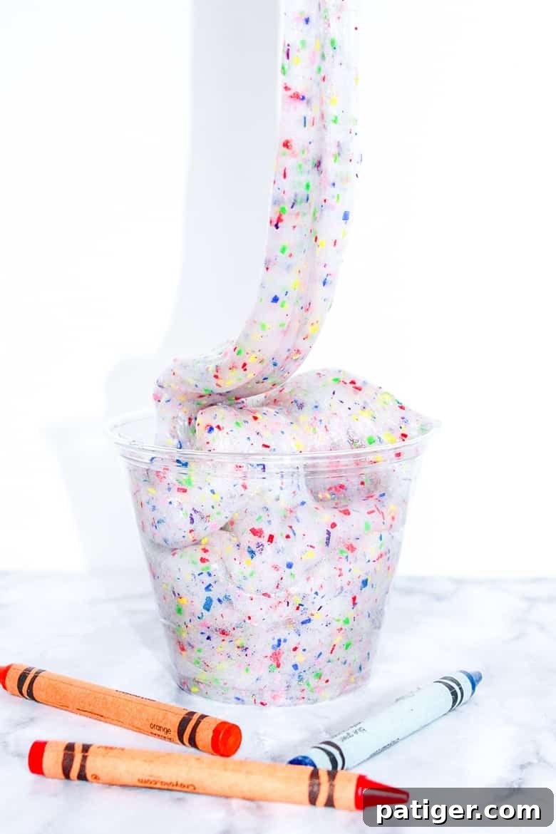 Colorburst Crayon Slime 7 A large batch of colorful crayon slime being stretched and played with on a clean surface. Showcases the final product of an easy DIY crayon slime recipe.