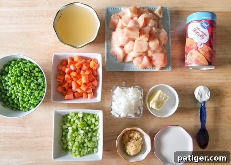 All ingredients for Instant Pot Chicken and Dumplings laid out: boneless chicken breasts, canned biscuits, olive oil, butter, garlic, onion, celery, carrots, frozen peas, heavy cream, chicken broth, cream of chicken soup, and poultry seasoning.