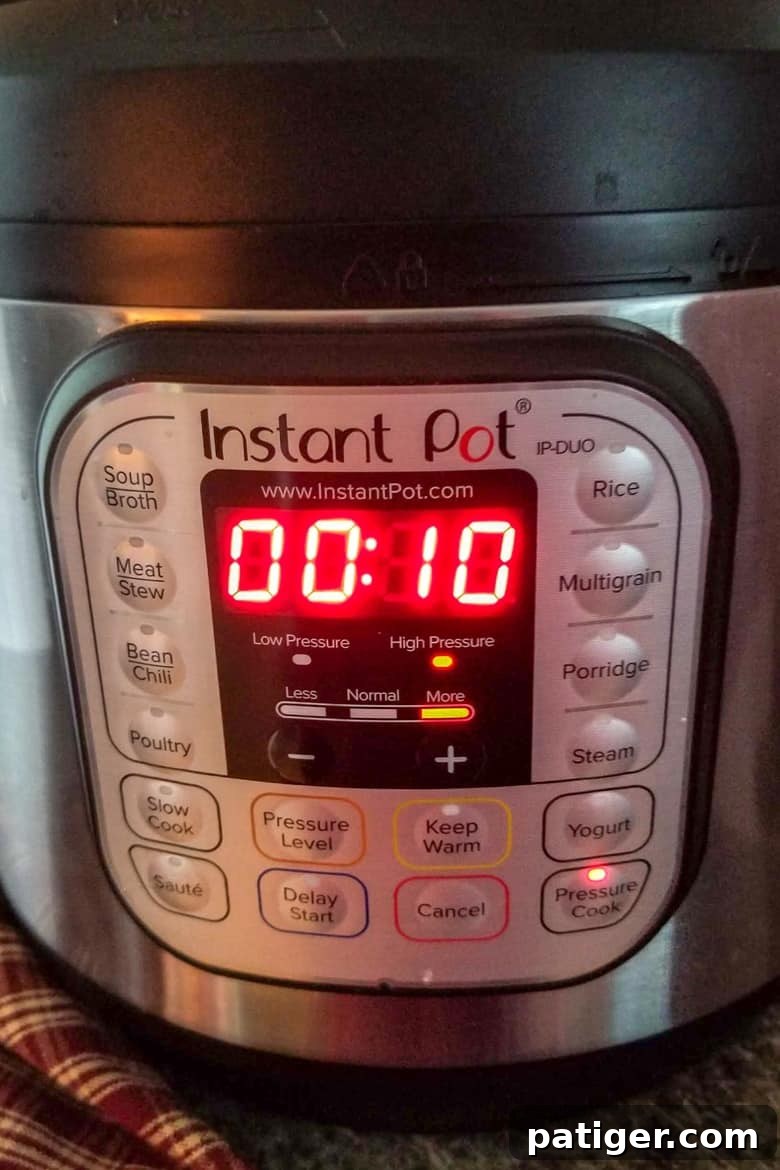 Instant Pot screen displaying '10 mins' on high pressure, with the lid closed and venting sealed, cooking the chicken and vegetable base.