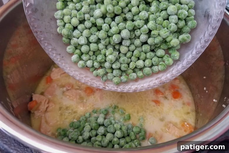 Fresh frozen peas being stirred into the cooked chicken and vegetable mixture in the Instant Pot, adding a vibrant color and fresh taste.