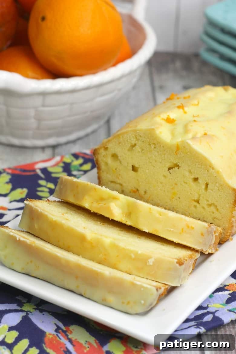 Glazed orange loaf cake on a white serving plate, with 3 slices cut, showcasing its moist texture and bright citrus glaze.