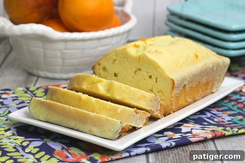 A delicious orange bread topped with a sweet orange glaze and with fresh orange slices in the background.