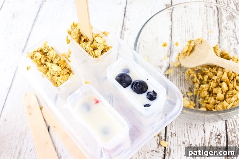 Frozen Yogurt Breakfast Bites 5 Popsicle mold filled with yogurt and berries. Some of the molds are topped with granola a well.