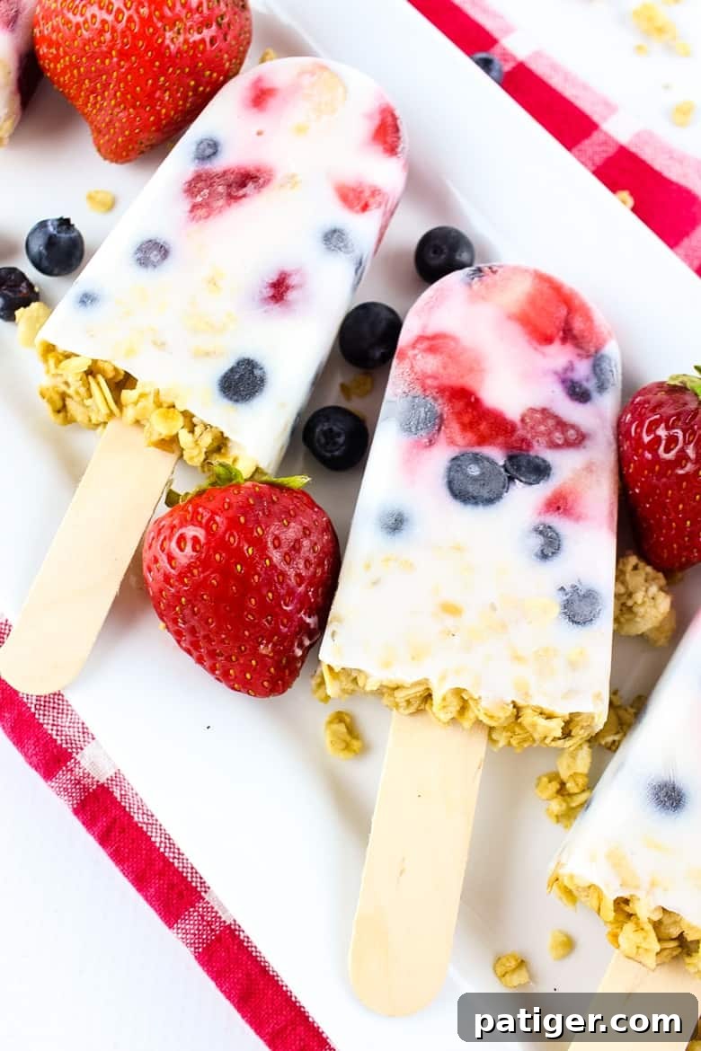 Frozen Yogurt Breakfast Bites 6 Yogurt, berry, and granola popsicles on a white platter, with fresh strawberries and blueberries