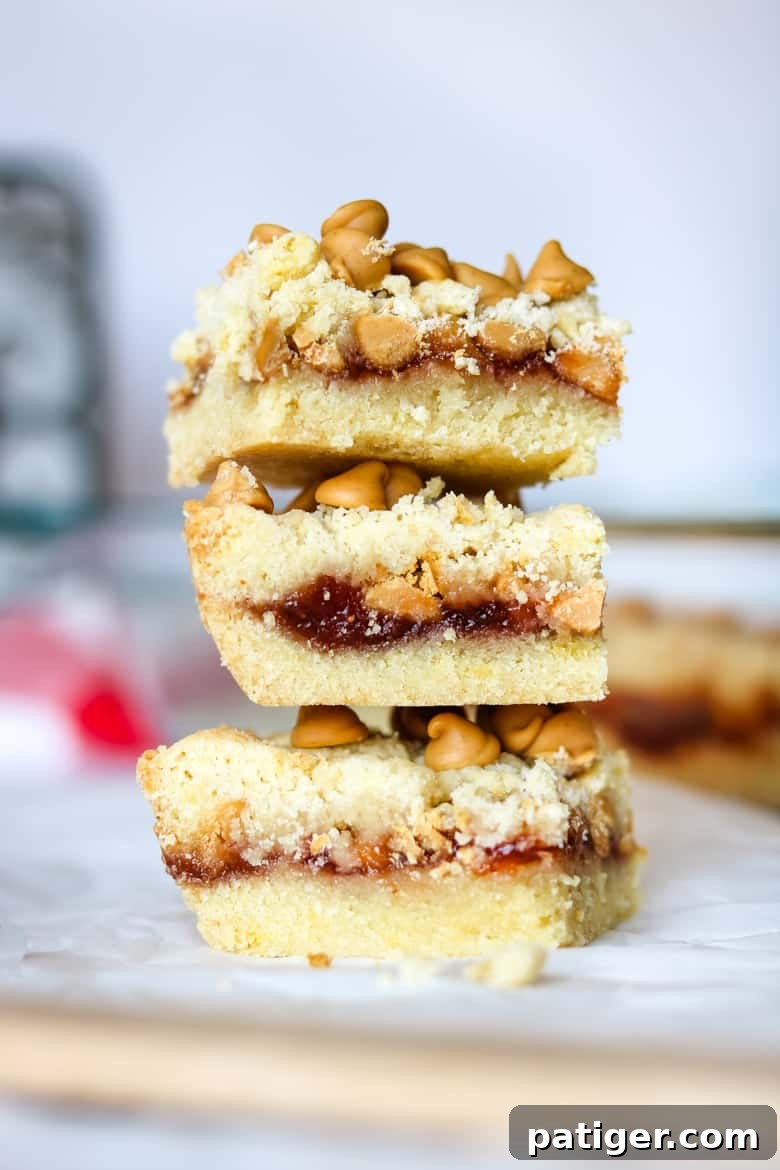 Three golden brown Peanut Butter and Jelly Bars stacked, revealing a sweet jelly layer and peanut butter chips