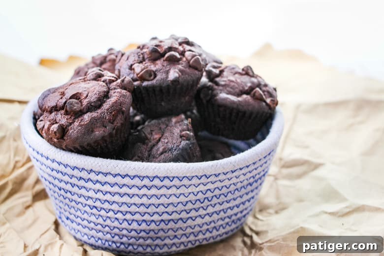 Decadent Double Chocolate Banana Muffins 3 Blue and white woven bowl filled with chocolate muffins with chocolate chips.