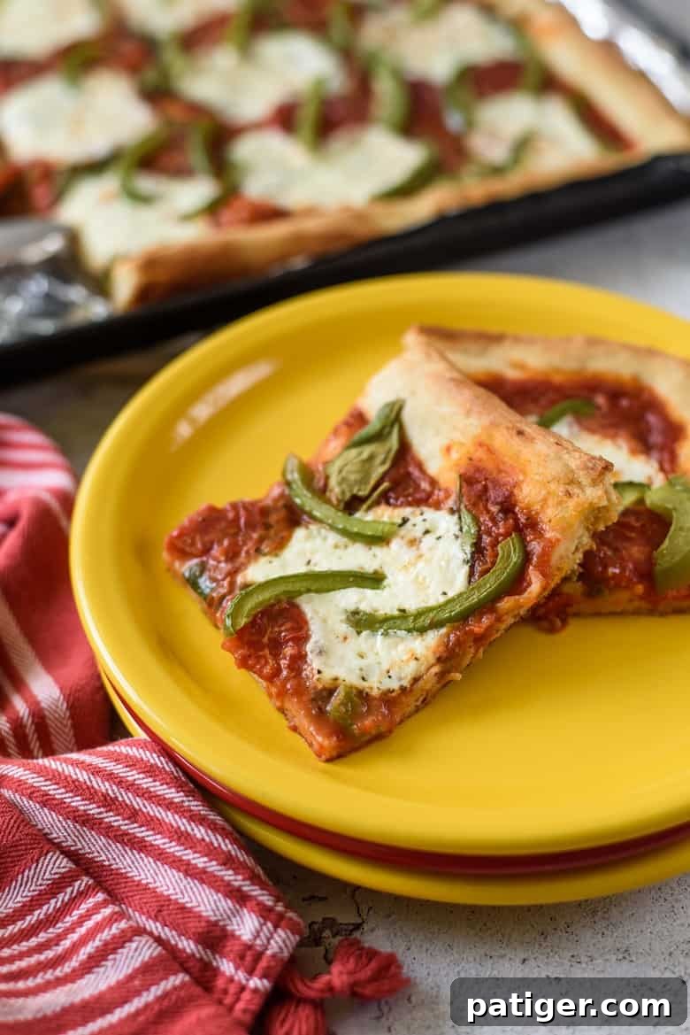 Effortless Sheet Pan Pizza 4 Two generous slices of Sheet Pan Pizza served on a bright yellow plate, with the rest of the pizza blurring in the background.