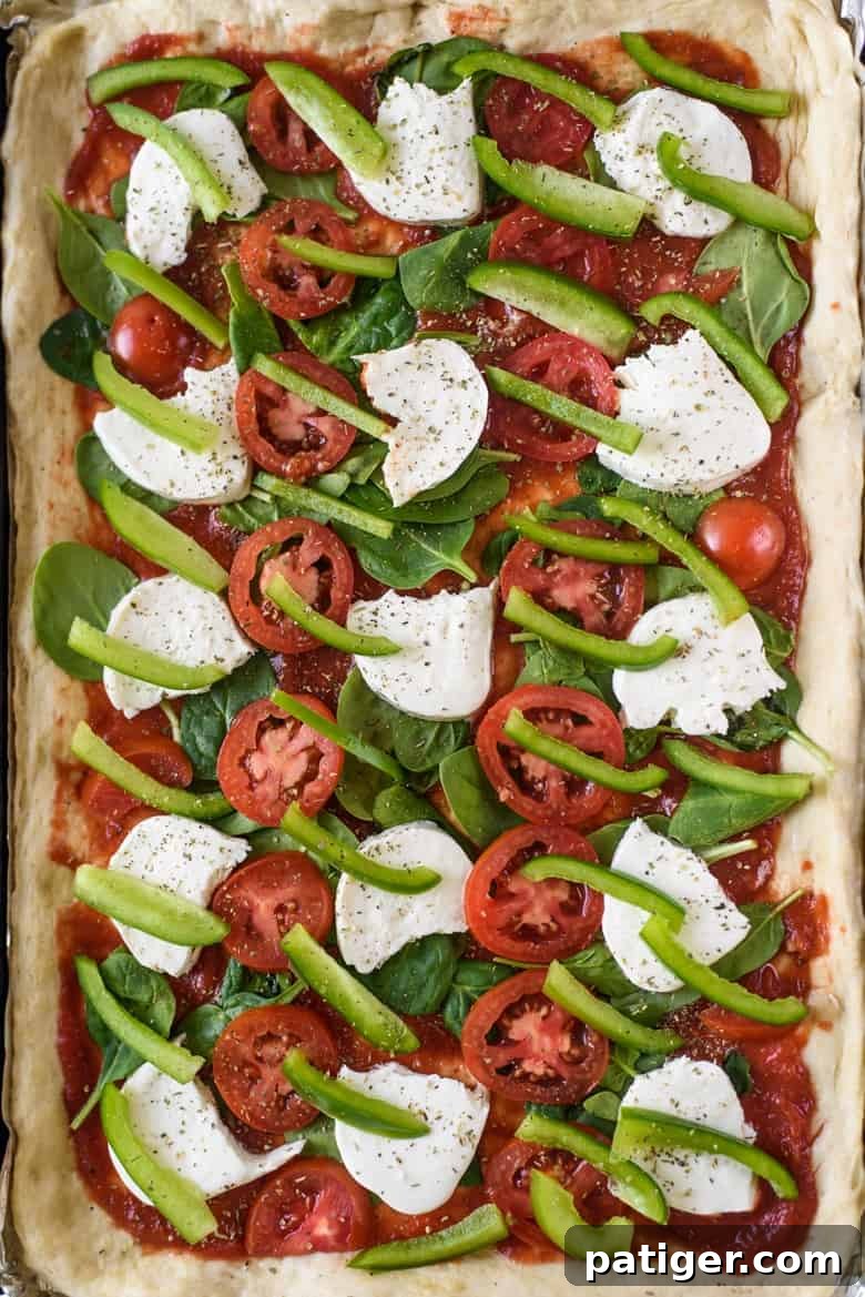 Effortless Sheet Pan Pizza 5 Unbaked pizza on a foil-lined sheet pan, ready for the oven with a generous layer of toppings.