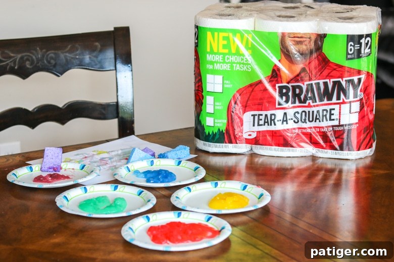Vibrant homemade paints on paper plates with sponges, paper, and Brawny® Tear-A-Square® paper towel packaging, ready for a toddler art session.