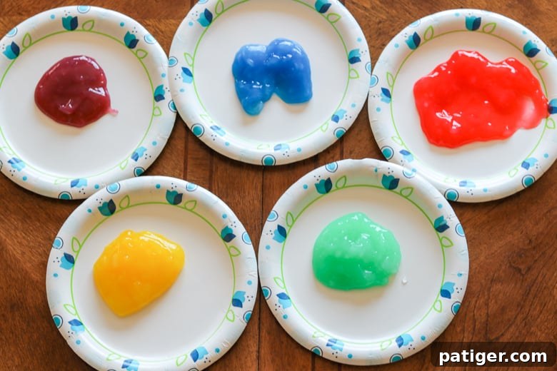 Five vibrant colors of homemade taste-safe paints – purple, blue, red, yellow, and green – neatly arranged on paper plates, ready for artistic exploration.