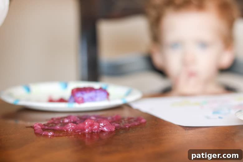 Purple paint splattered on a dining table, with a child visible in the blurred background, illustrating a common toddler art mess.