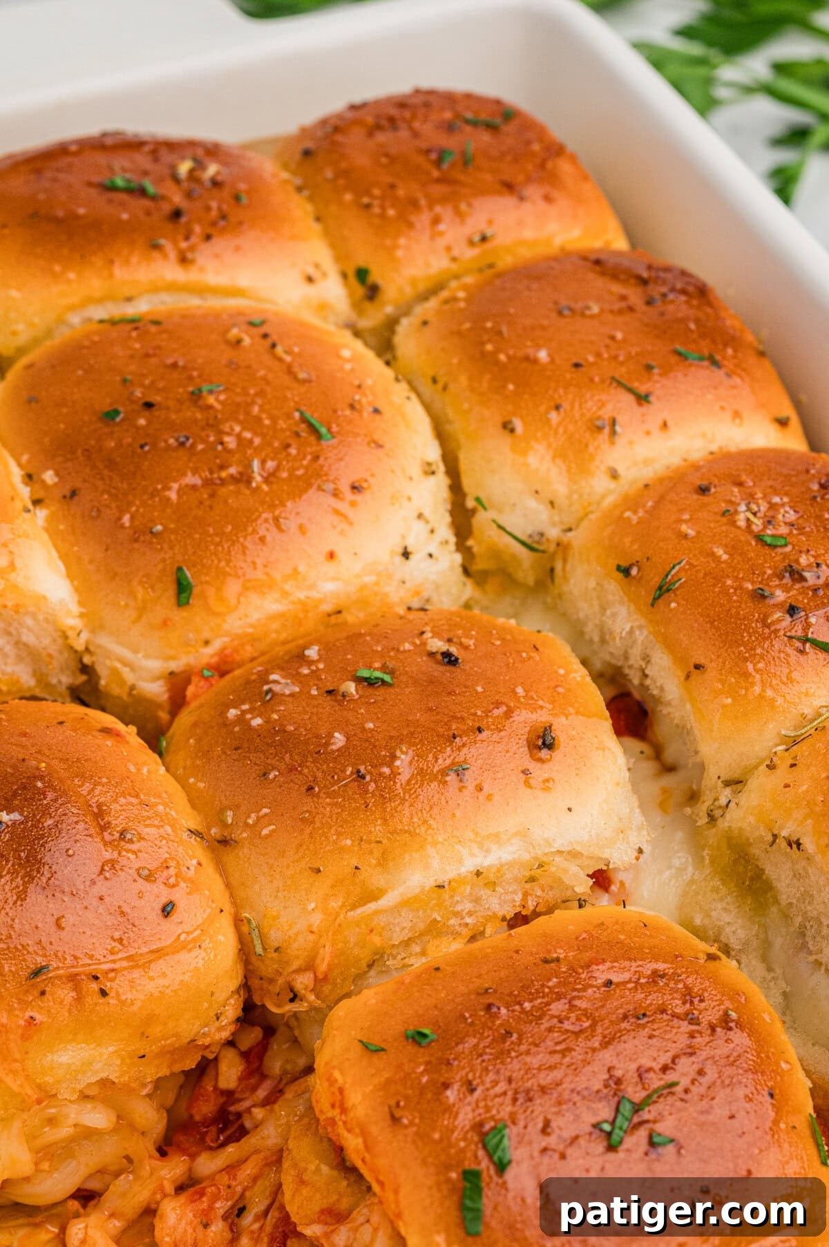 Golden brown chicken parmesan sliders topped with herbs, with melted cheese peeking from the edges, arranged in a row.