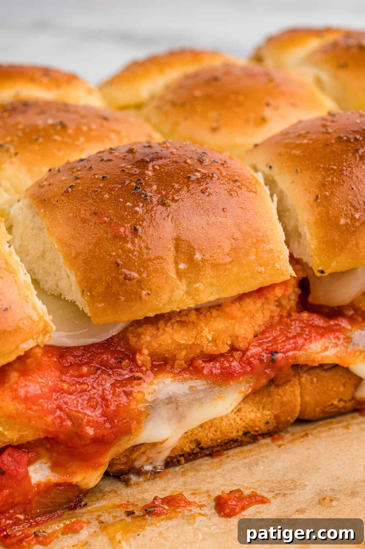 Close-up of golden brown chicken parm sliders with nuggets in a row, showing layers of breaded chicken, marinara sauce, and melted mozzarella between soft, herb-topped buns.