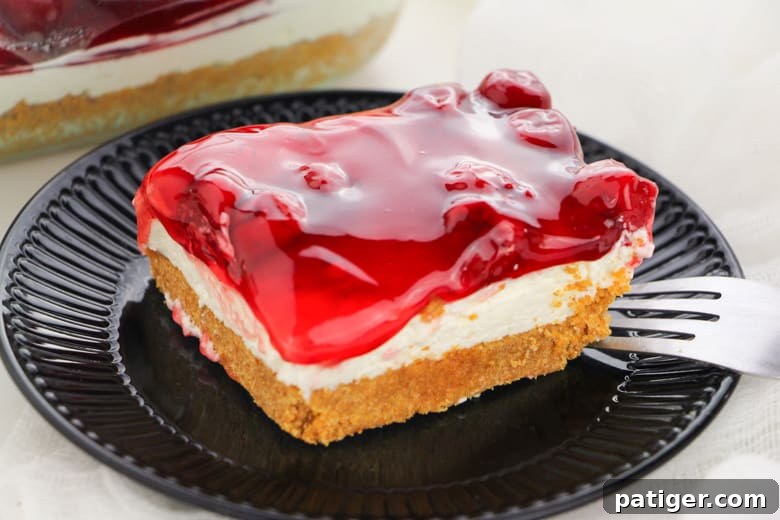 A slice of No Bake Cherry Cheesecake presented on a white plate, showcasing its distinct layers.