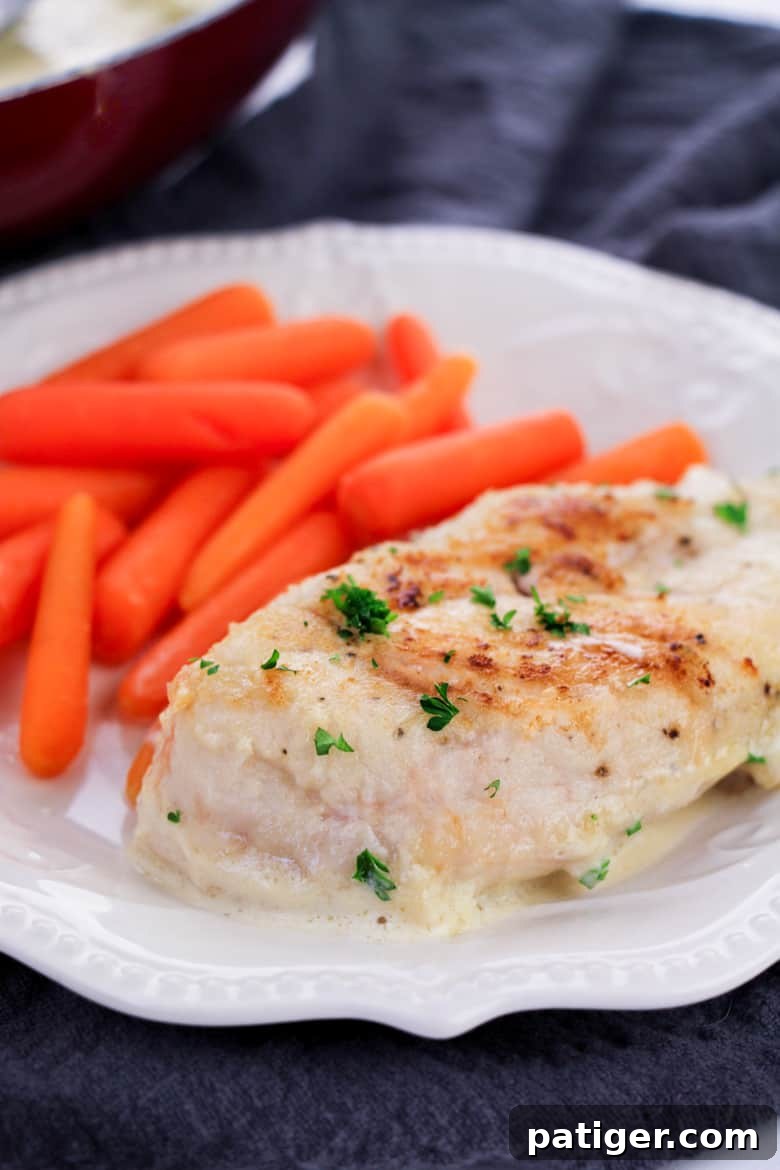 Creamy garlic chicken breast and cooked baby carrots on a white dinner plate.