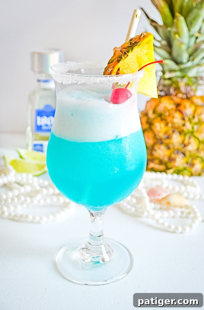 Ocean Siren Margarita Freeze 2 Frozen blue cocktail garnished with fresh pineapple and maraschino cherry, representing a Mermaid Margarita