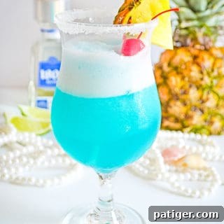 Frozen blue cocktail garnished with fresh pineapple and maraschino cherry