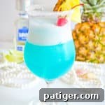 Frozen blue cocktail garnished with fresh pineapple and maraschino cherry