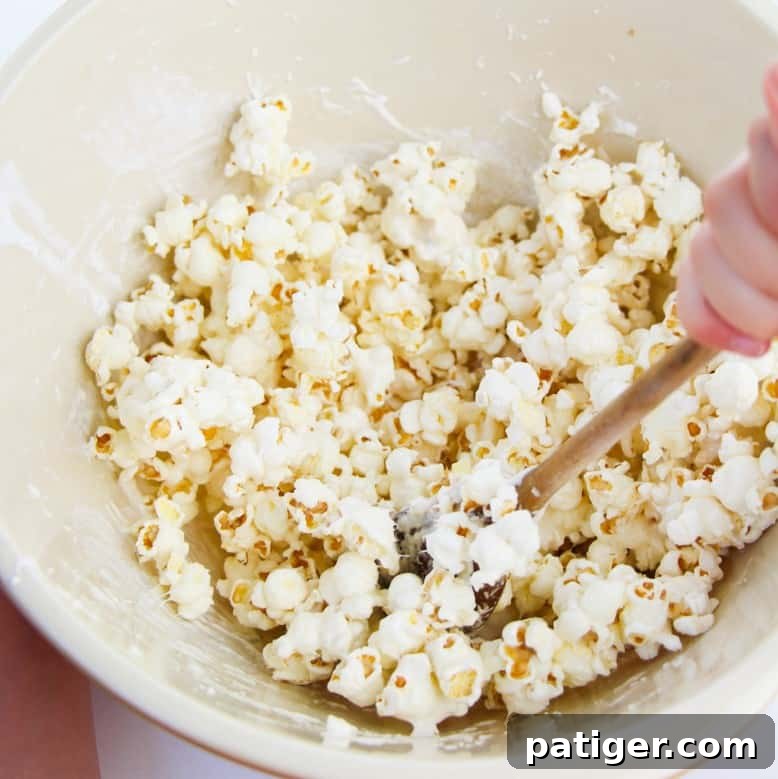 A large bowl filled with popcorn being gently mixed, ensuring each kernel is coated in the sweet marshmallow fluff, preparing it for the cake batter transformation.