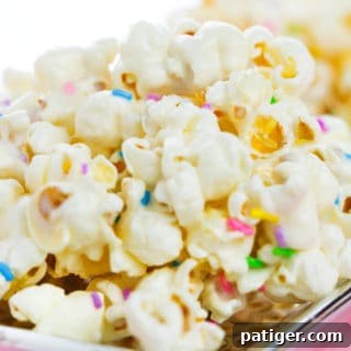 Cake batter popcorn topped with rainbow sprinkles and served on a flat silver plate.