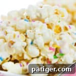 Cake batter popcorn topped with rainbow sprinkles and served on a flat silver plate.