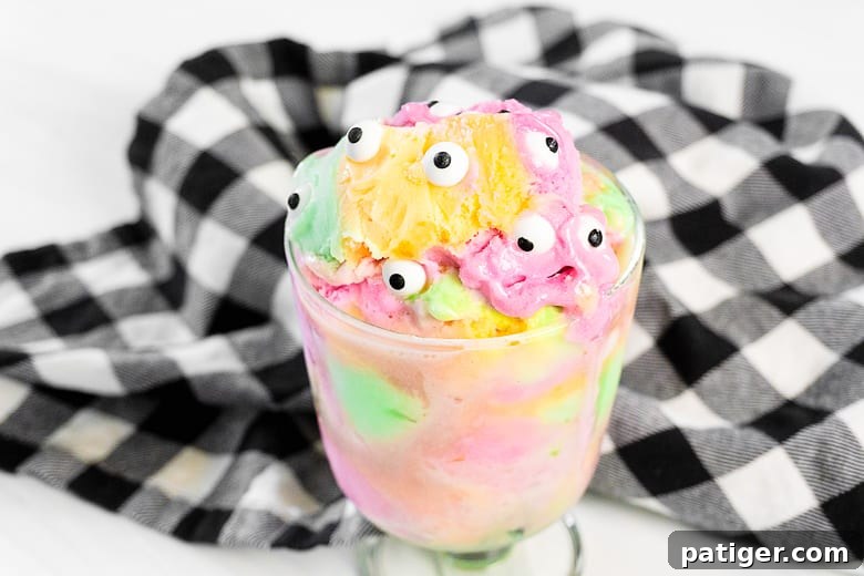 A close-up of a Monster Sherbet Halloween Sundae, featuring a vibrant swirl of rainbow sherbet adorned with whimsical candy eyeballs.