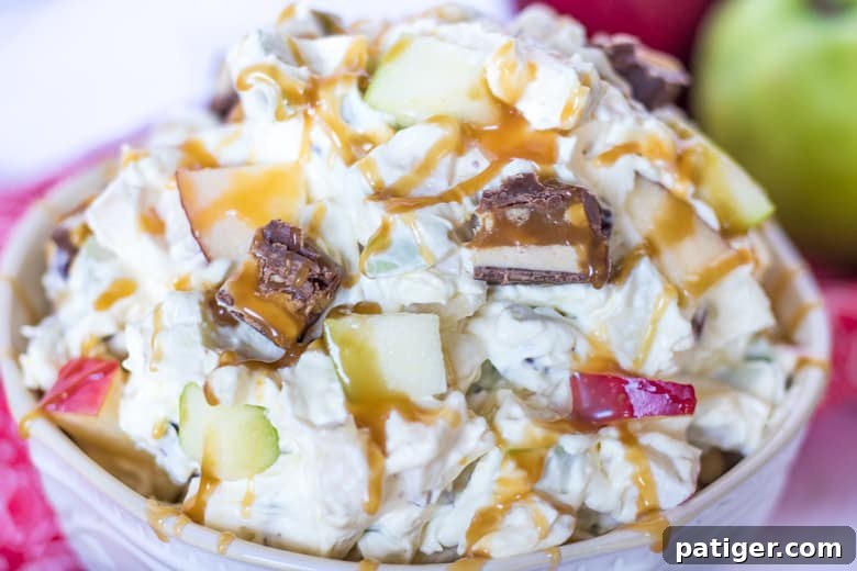 Ultimate Snickers Caramel Apple Salad 3 Close-up of Apple Snickers Salad in a white serving bowl, showcasing generous chunks of Snickers candy bars, vibrant red and green apple pieces, all enveloped in a rich, creamy dressing, ready to be enjoyed.
