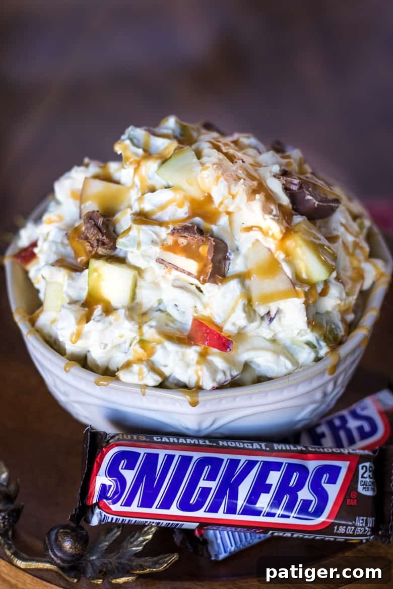 Ultimate Snickers Caramel Apple Salad 4 A side view of the Snickers Salad artfully arranged in a white bowl, with whole Snickers bars placed decoratively beside it, emphasizing the key ingredient of this sweet treat.