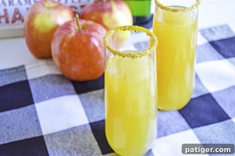 A close-up shot of two apple cider mimosas on a table, garnished with fresh apple slices and a sugared rim.