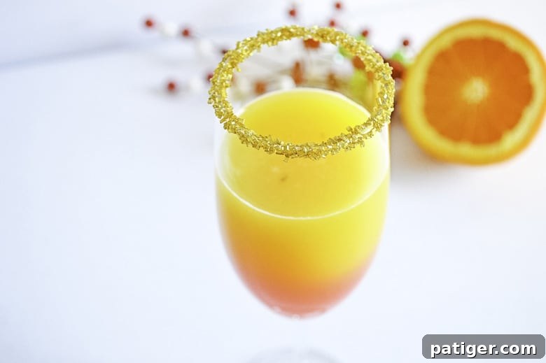 Close-up of a festive Christmas Mimosa cocktail, showcasing the beautiful red and orange layers with a sugared rim