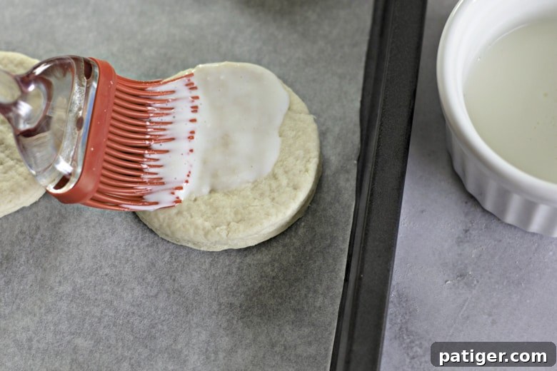 Fluffy Buttermilk Biscuits from Scratch 12 A pastry brush applying a thin layer of buttermilk to the tops of raw biscuit dough before baking.