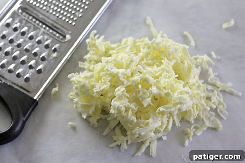 Fluffy Buttermilk Biscuits from Scratch 5 Close-up of hands grating cold butter into a bowl using a cheese grater, preparing it for buttermilk biscuits.