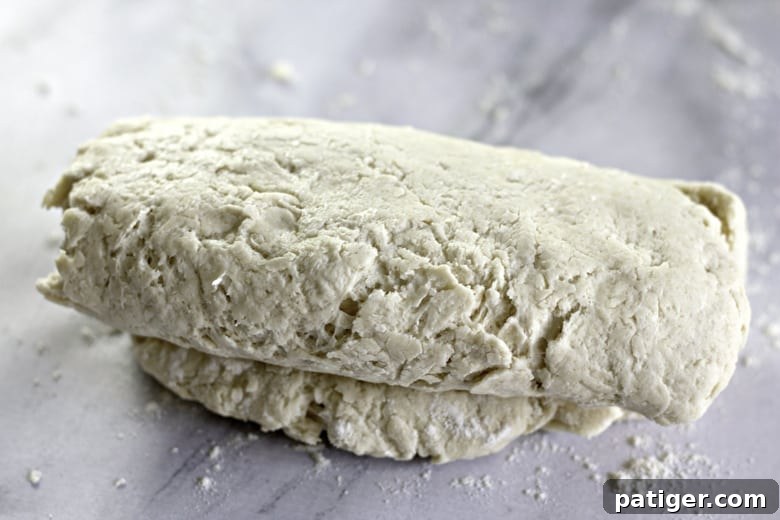 Fluffy Buttermilk Biscuits from Scratch 9 Hands demonstrating the letter-folding technique on biscuit dough on a lightly floured surface to create layers.