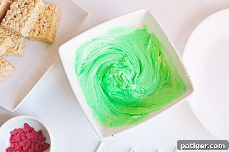 Grinch's Green Krispie Delights 5 Melted green chocolate, red heart sprinkles, and unwrapped Rice Krispie treats, set up for dipping.