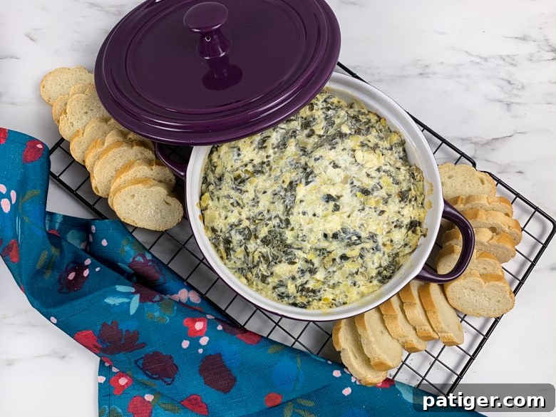 A warm, bubbly spinach and artichoke dip served in a rustic ceramic dish, surrounded by toasted slices of baguette for dipping.