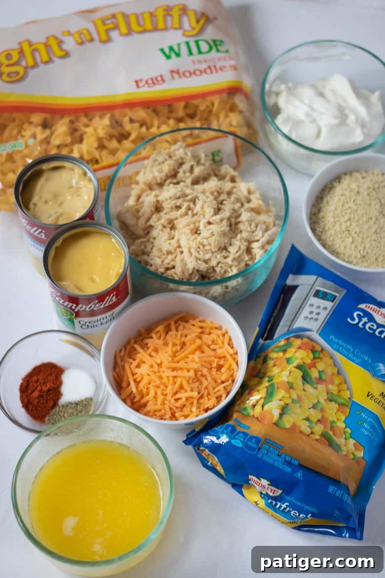 Ingredients for Easy Chicken Noodle Casserole: frozen mixed vegetables, shredded chicken, egg noodles, cream of chicken soup, shredded cheese, bread crumbs, sour cream, melted butter, and seasonings.