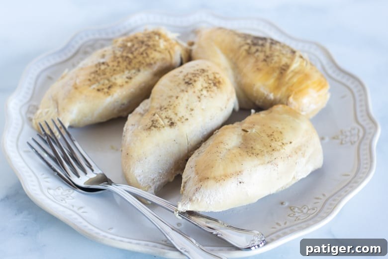 4 cooked chicken breasts on white plate with two forks