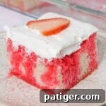 Strawberry Infusion Poke Cake 11 Square slice of strawberry jello poke cake made from white cake with red Jello drips through it. The cake is topped with cool whip topping and a slice of strawberry.