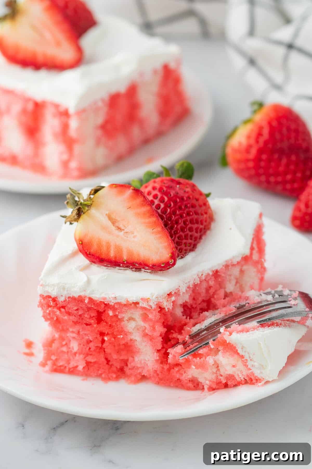 Strawberry Infusion Poke Cake 8 A fork taking a piece from a plated slice of strawberry Jello poke cake, showing the moist cake, red Jello streaks, and creamy whipped topping.