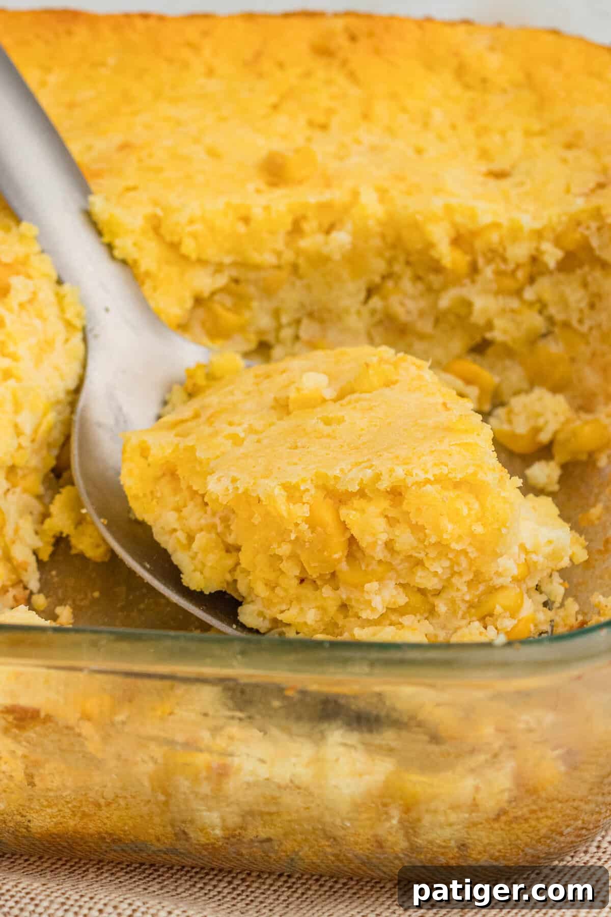 Golden Jiffy Cornbread and Creamed Corn Bake 2 Serving spoon scooping a generous portion of golden-brown Jiffy cornbread casserole with visible creamed corn and kernels.
